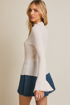 Woman wearing a mock neck ribbed knit top with flared sleeves against a beige background