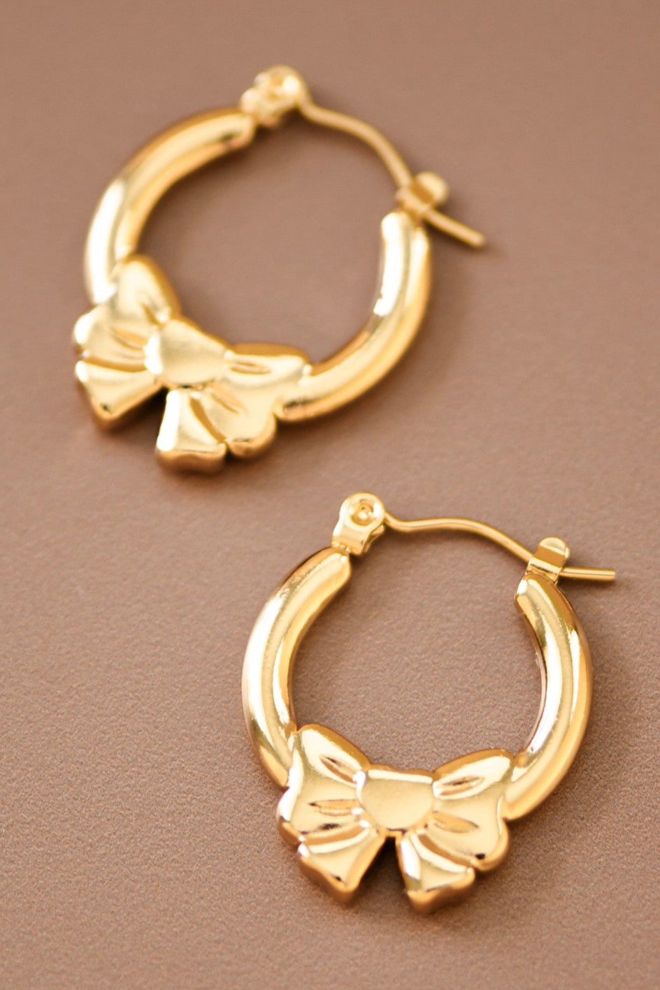 18k gold hoop earrings with bow design on a brown background