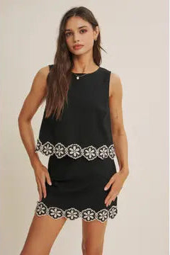 Black skort with white crochet floral pattern and matching top on a beige background