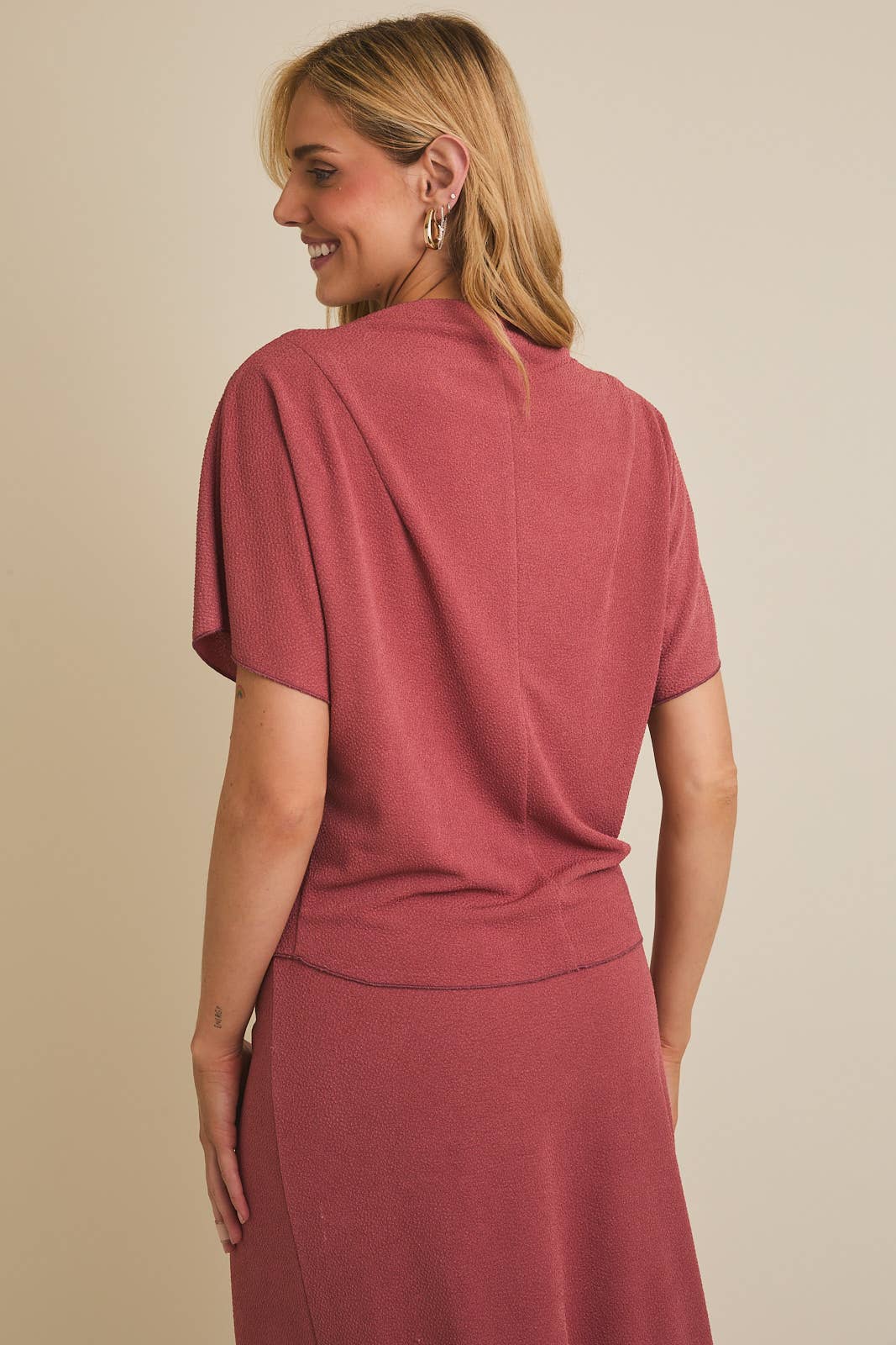 Back view of a woman wearing a mauve mock neck  top against a beige background