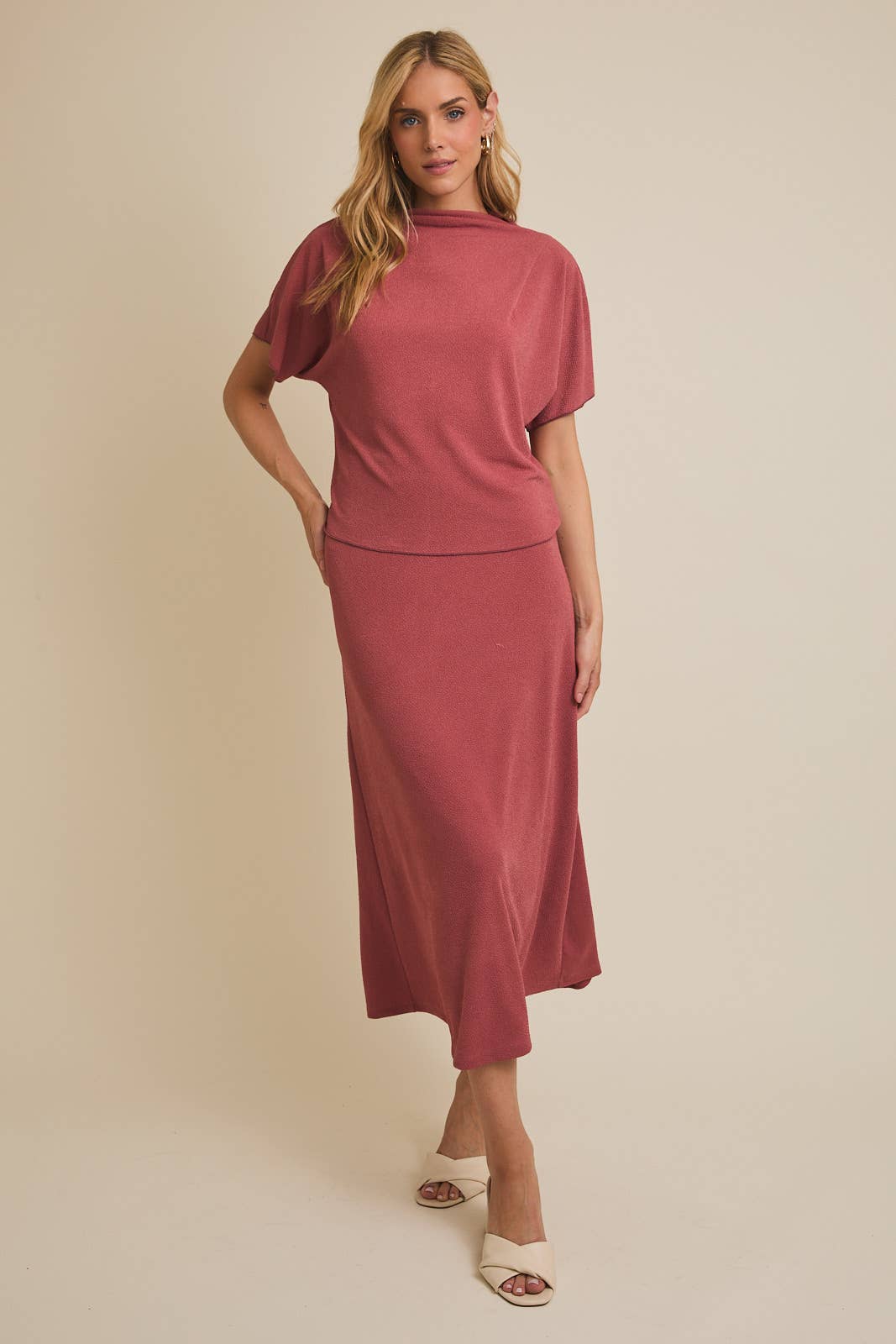 Woman wearing a mauve mock neck  top and matching skirt against a beige background