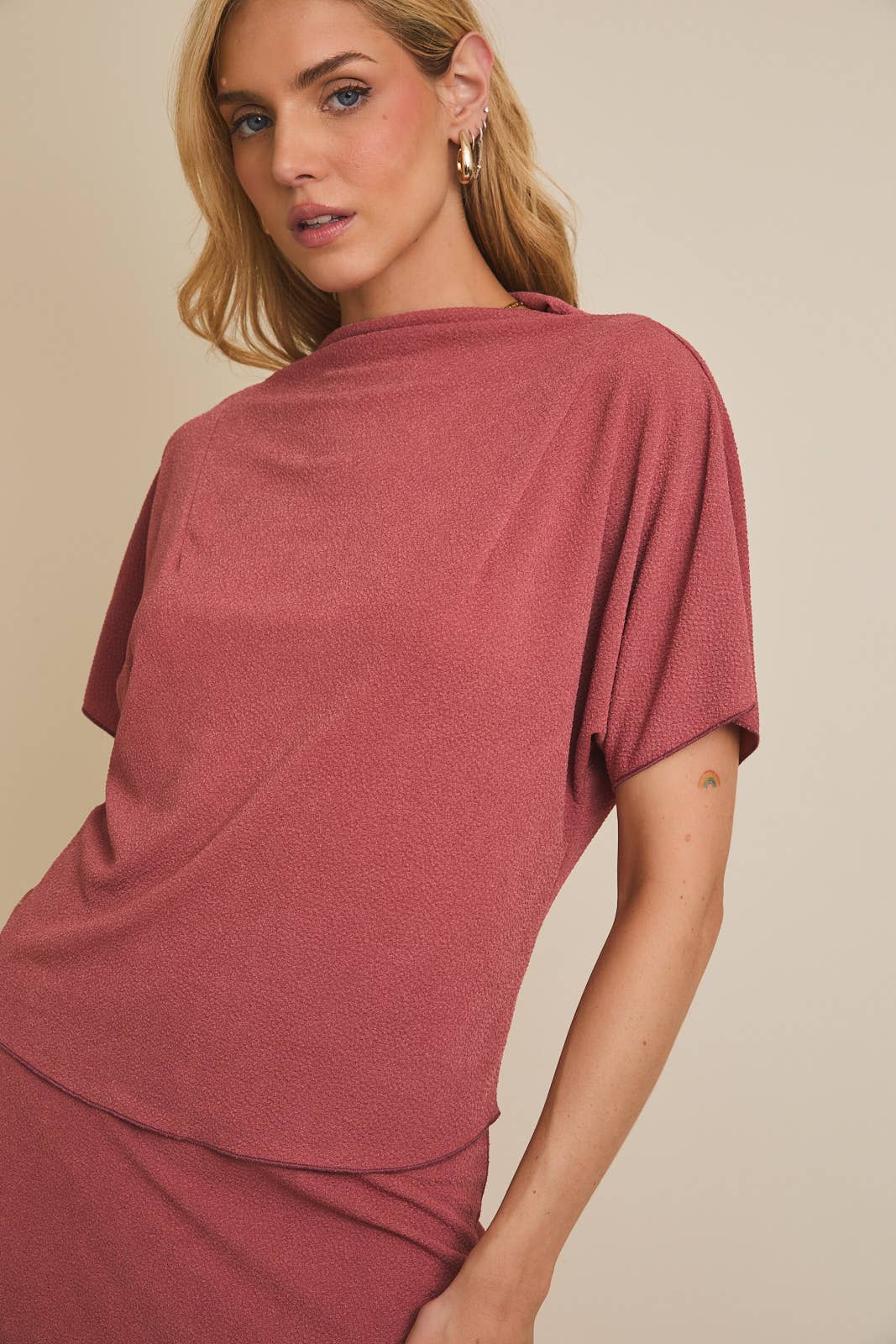 Woman wearing a mauve mock neck  top against a beige background