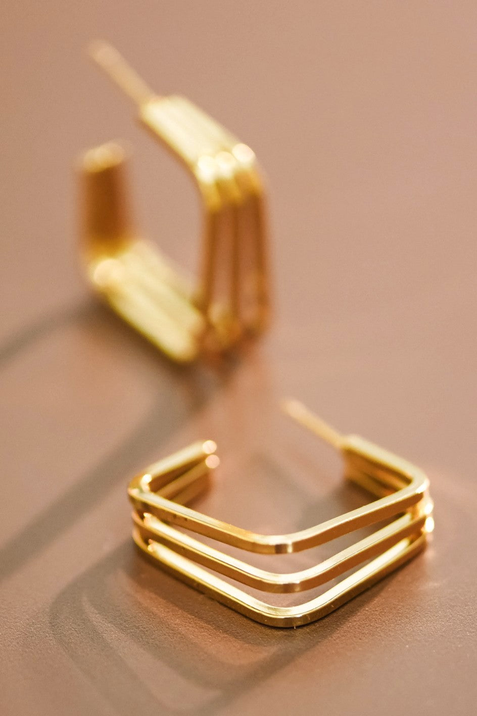 18k gold-plated triple hoop earrings on a reflective surface with a blurred background