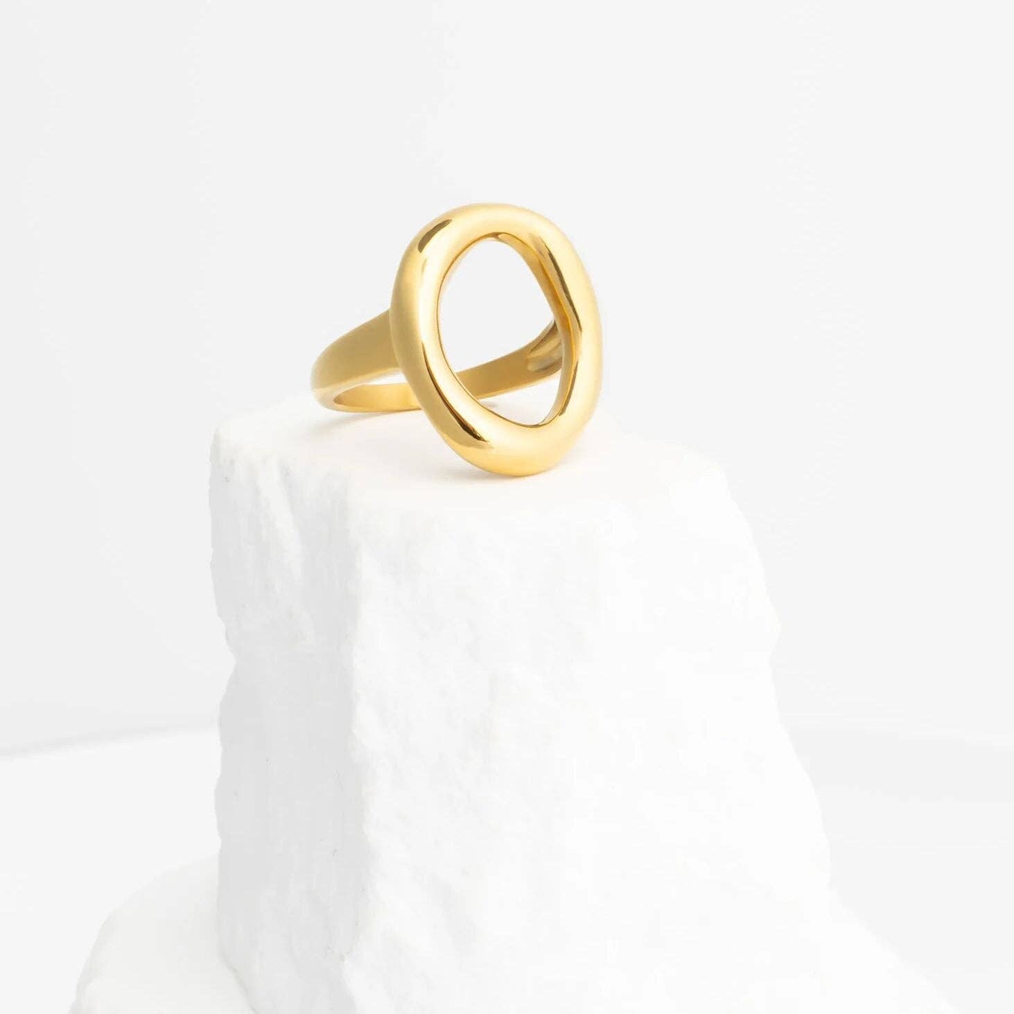Gold ring with oval motif design on a white marble surface