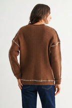 Back view of a woman wearing a chocolate brown sweater with white contrasting trim on a white background