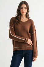 Woman wearing a chocolate brown sweater with white contrasting trim on a white background