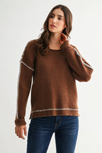 Woman wearing a chocolate brown sweater with white contrasting trim on a white background