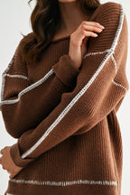 Woman wearing a chocolate brown sweater with white contrasting trim on a white background
