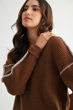 Woman wearing a chocolate brown sweater with white contrasting trim on a white background