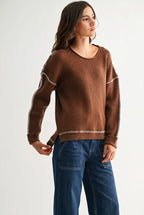 Woman wearing a chocolate brown sweater with white contrasting trim on a white background