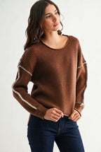 Woman wearing a chocolate brown sweater with white contrasting trim on a white background