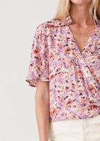 Woman wearing a floral wrap top with side tie and white shorts on a plain background