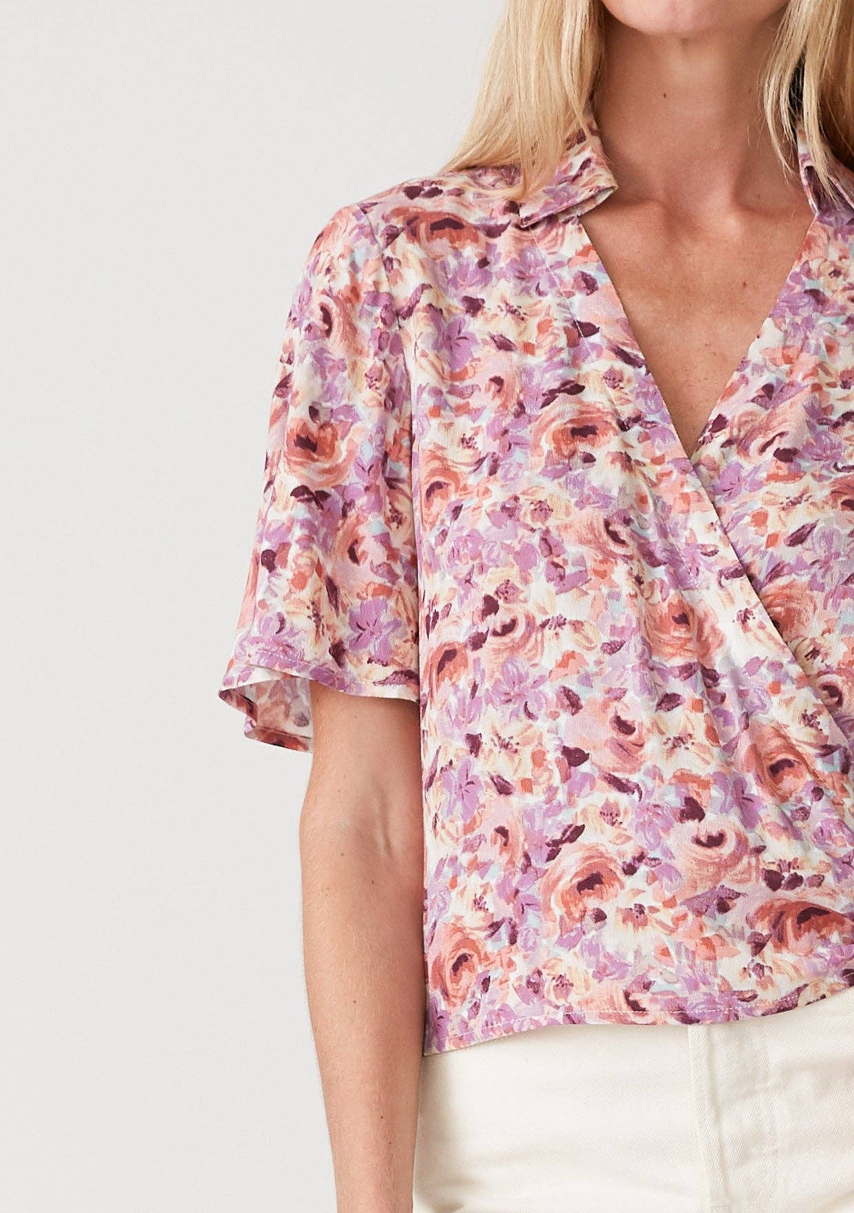 Woman wearing a floral wrap top with side tie and white shorts on a plain background
