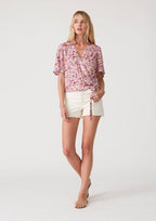 Woman wearing a floral wrap top with side tie and white shorts on a plain background