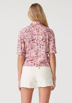 Back view of a woman wearing a floral wrap top with side tie and white shorts on a plain background