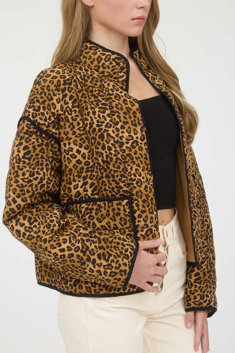 Woman wearing a leopard print puffer jacket over a black top and white pants on a white background