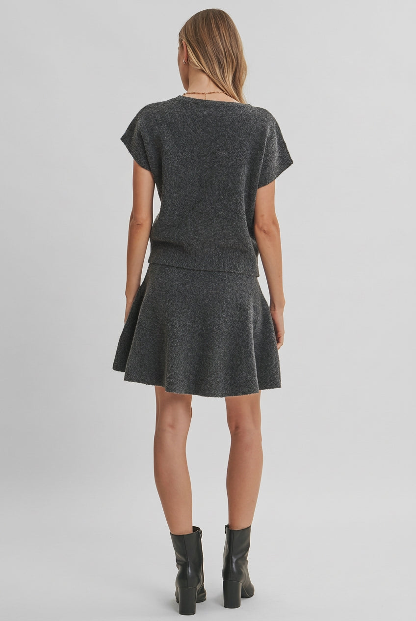 Back view of a woman modeling a charcoal knit dolman short-sleeve top and a matching flared skirt against a solid light beige background.