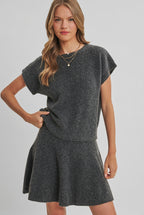 A woman modeling a charcoal knit dolman short-sleeve top and a matching flared skirt against a solid light beige background.
