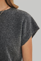 Closeup of a woman modeling a charcoal knit dolman short-sleeve top against a solid light beige background.