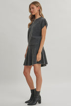 A woman modeling a charcoal knit dolman short-sleeve top and a matching flared skirt against a solid light beige background.