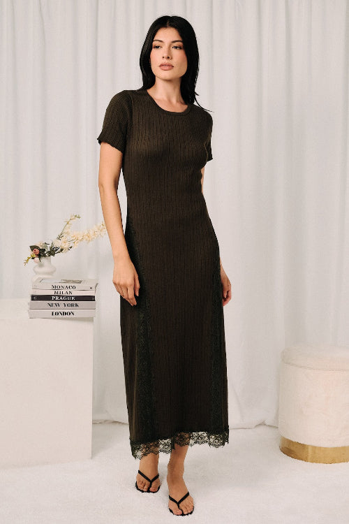 A woman models an olive short-sleeve midi dress with a ribbed texture and lace insert on the skirt and hem, standing in front of a white curtain backdrop.