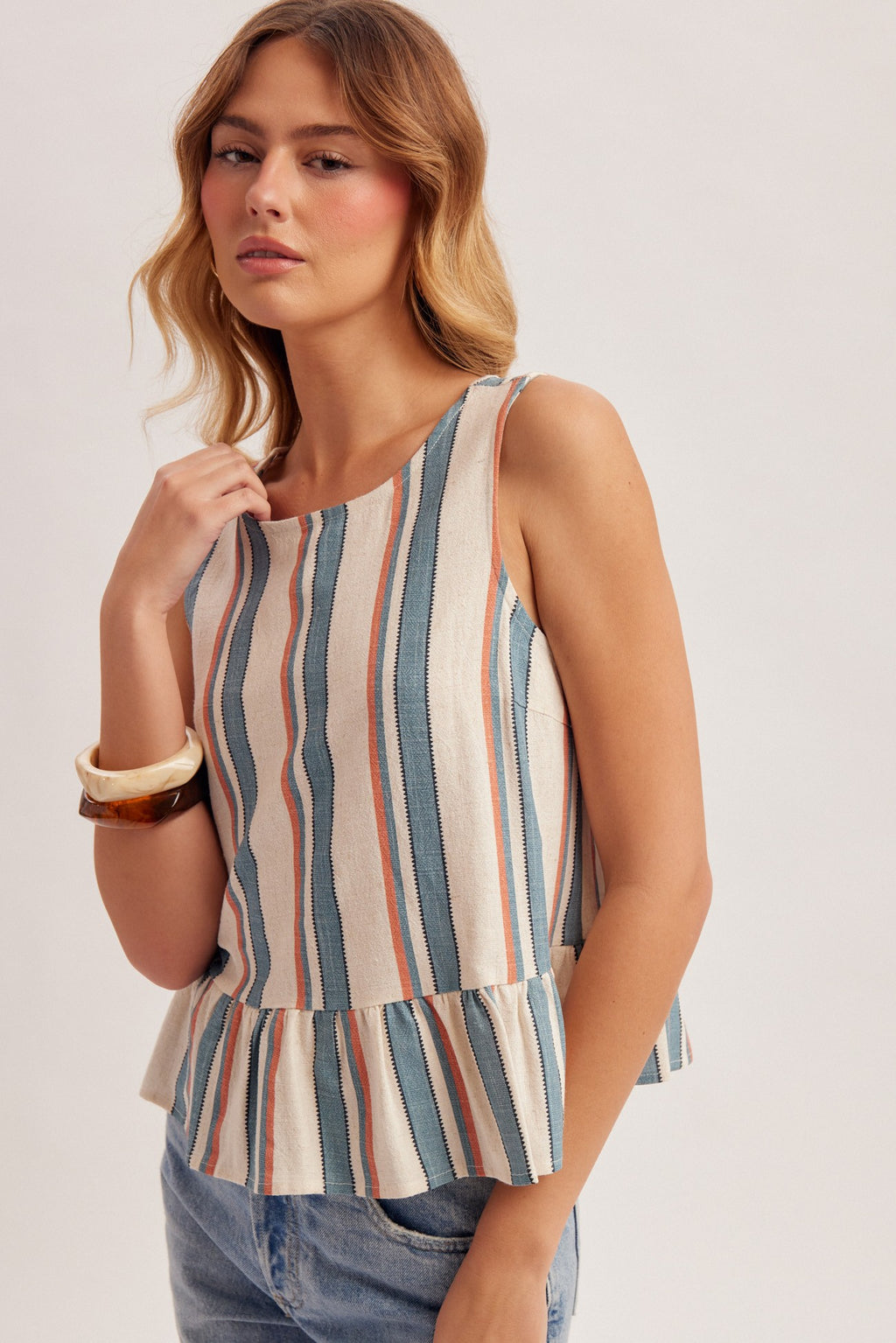 Woman wearing a striped blue, red and cream tank top with jeans on a plain background