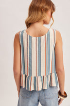 Back view of a woman wearing a striped blue, red and cream tank top with jeans on a plain background