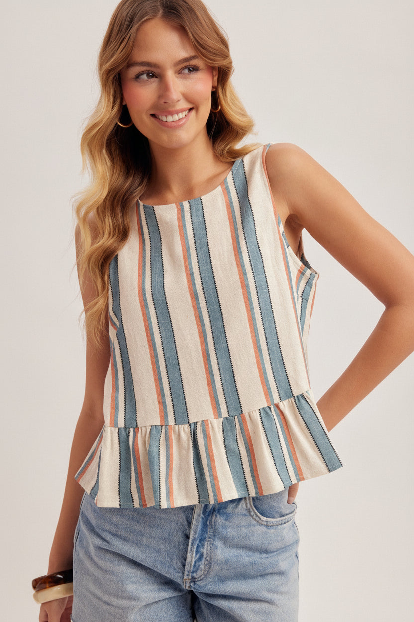 Woman wearing a striped blue, red and cream tank top with jeans on a plain background