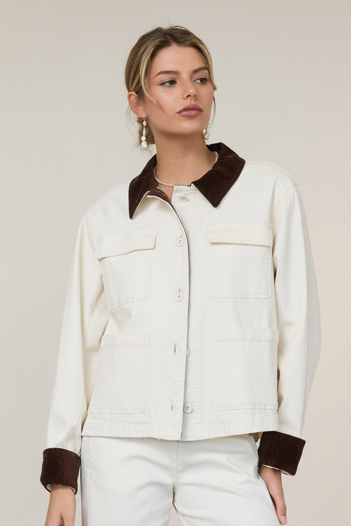 Woman in a white barn jacket with brown accents standing against a grey wall