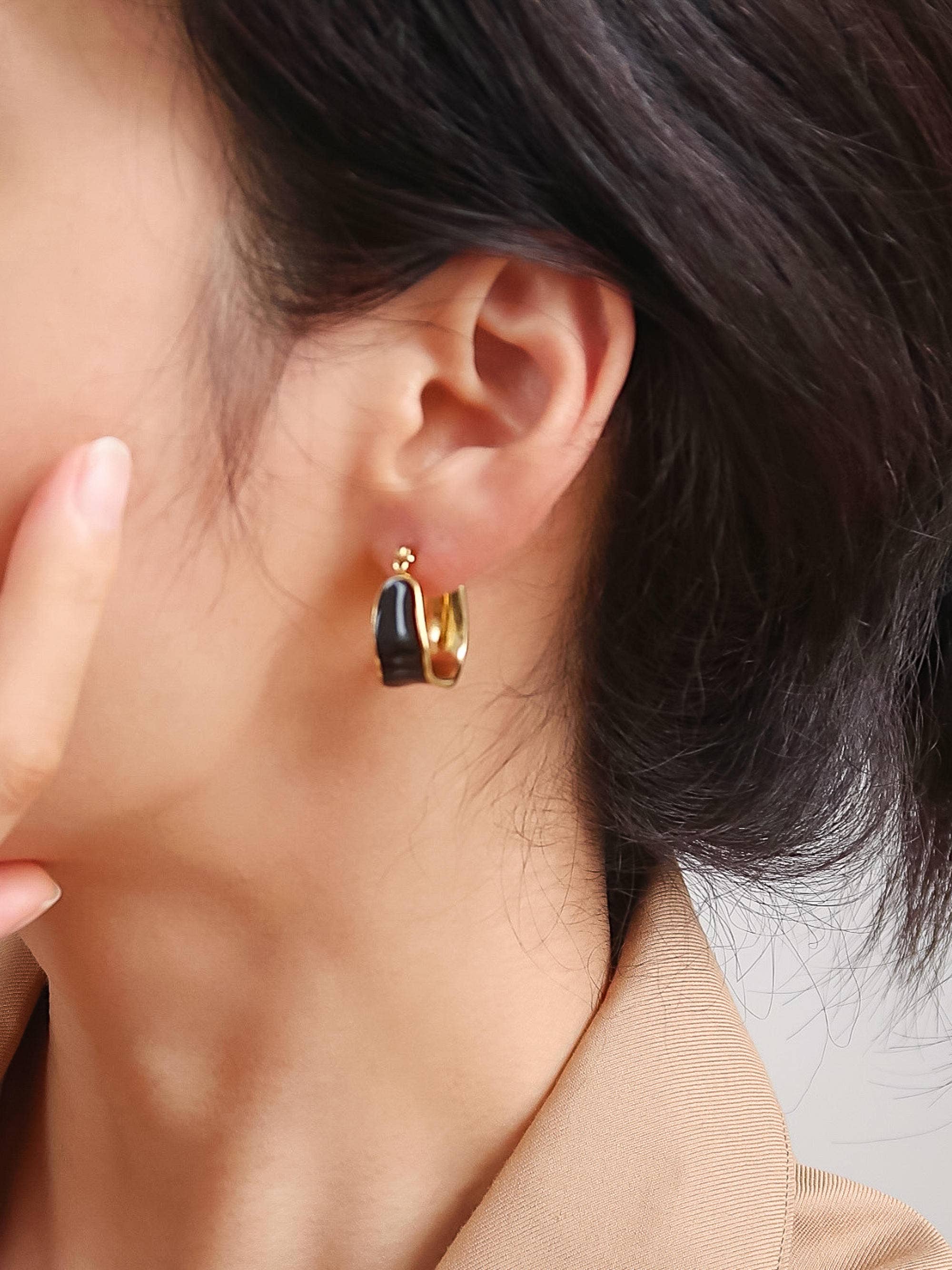 Close-up of a person wearing women's gold hoop earrings with a black enamel center
