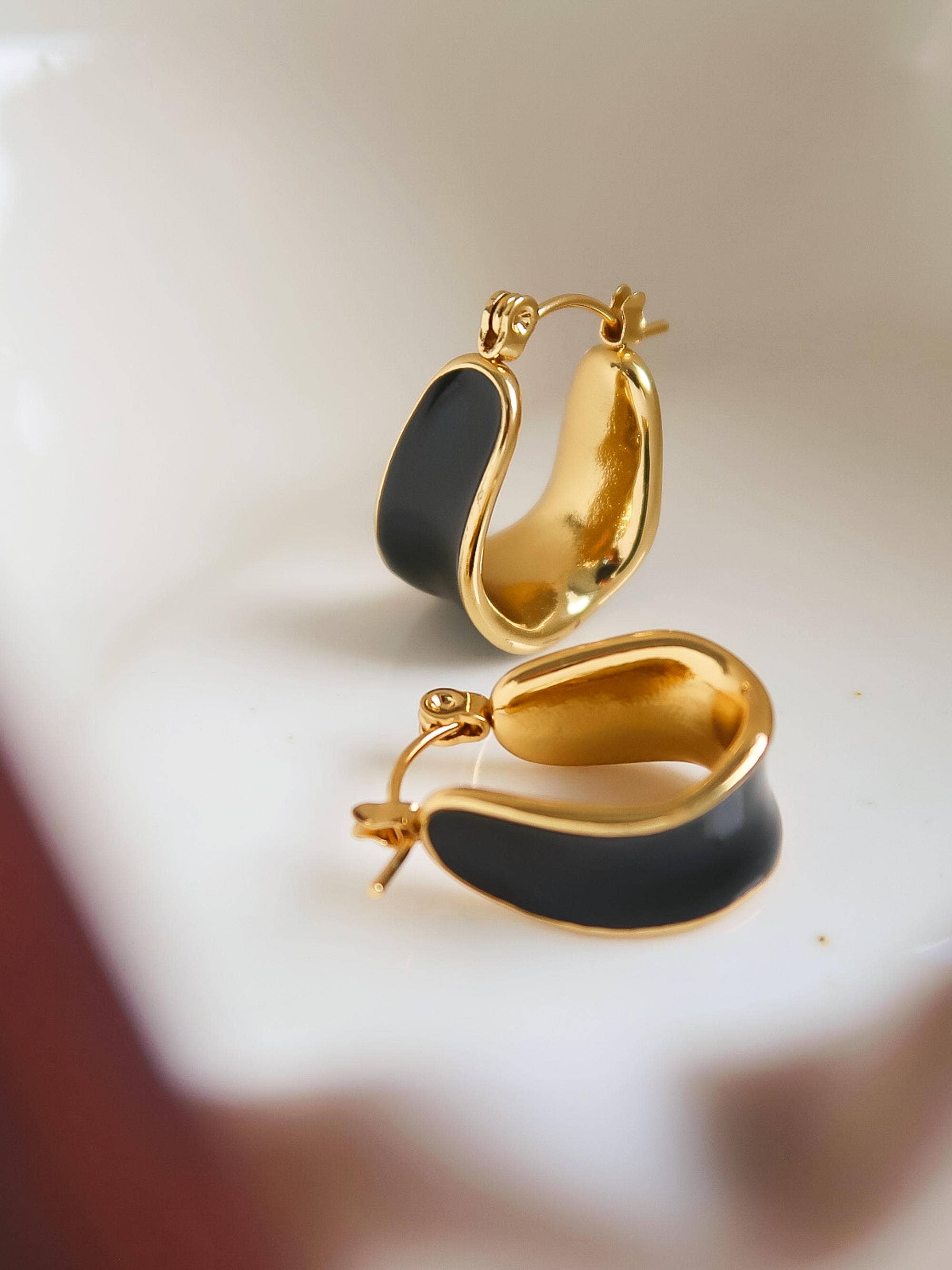 Women's gold hoop earrings with black enamel center on a light background
