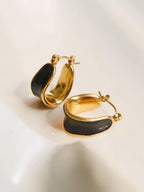Women's gold hoop earrings with black enamel center on a light background