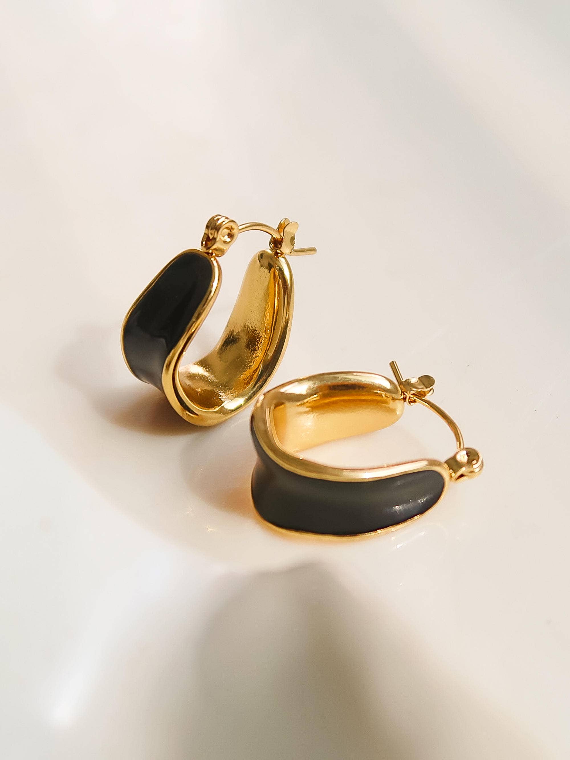 Women's gold hoop earrings with black enamel center on a light background