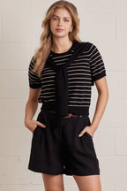 A woman wearing a striped short sleeve knit top with an attached layered shoulder shirt style against a grey background
