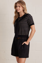 A woman wearing a striped short sleeve knit top with an attached layered shoulder shirt style against a grey background