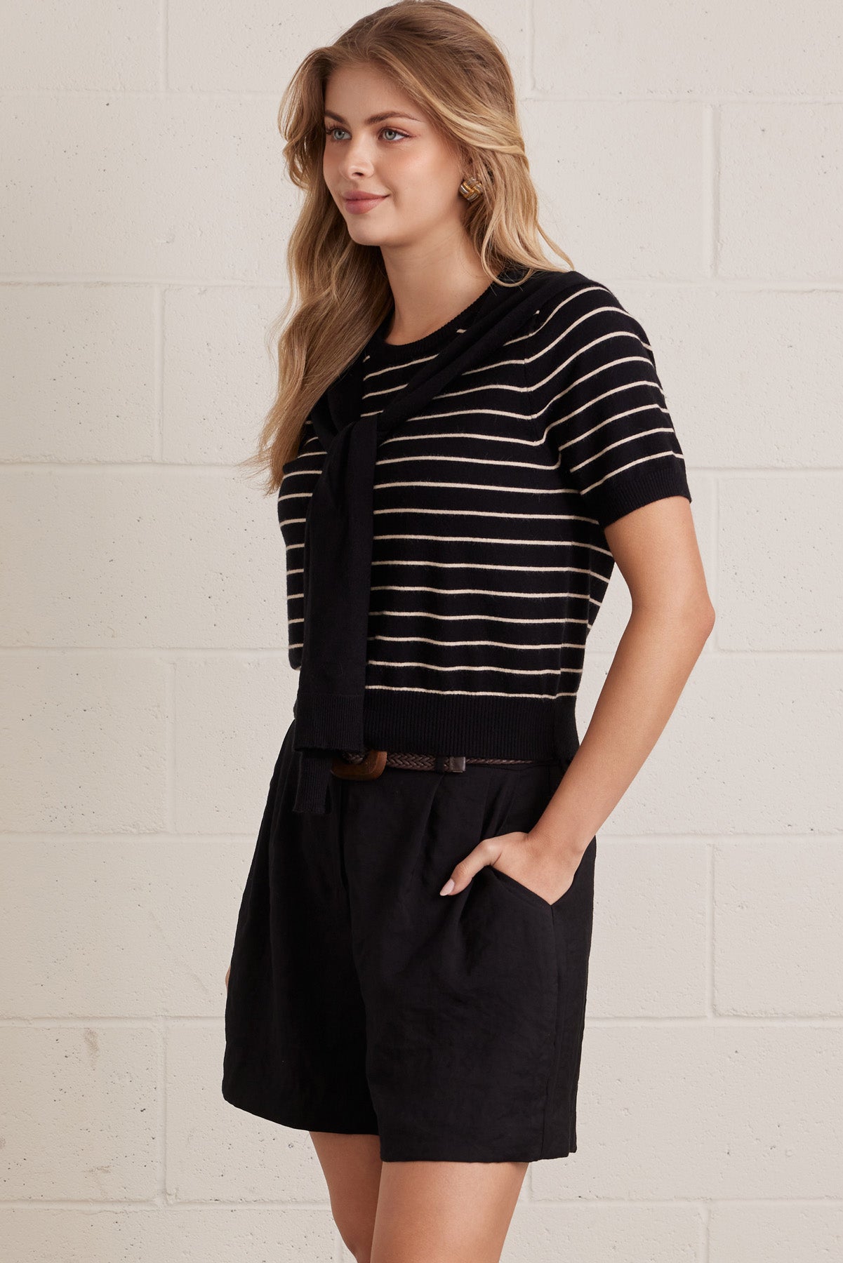 A woman wearing a striped short sleeve knit top with an attached layered shoulder shirt style against a grey background