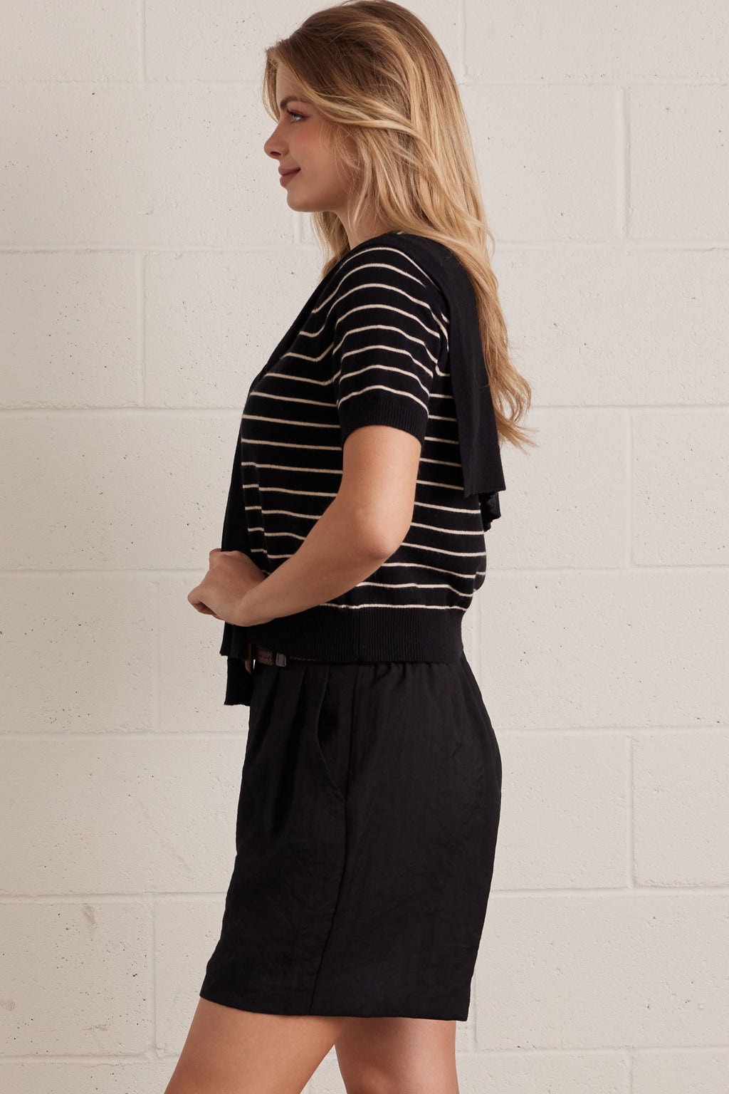 A woman wearing a striped short sleeve knit top with an attached layered shoulder shirt style against a grey background
