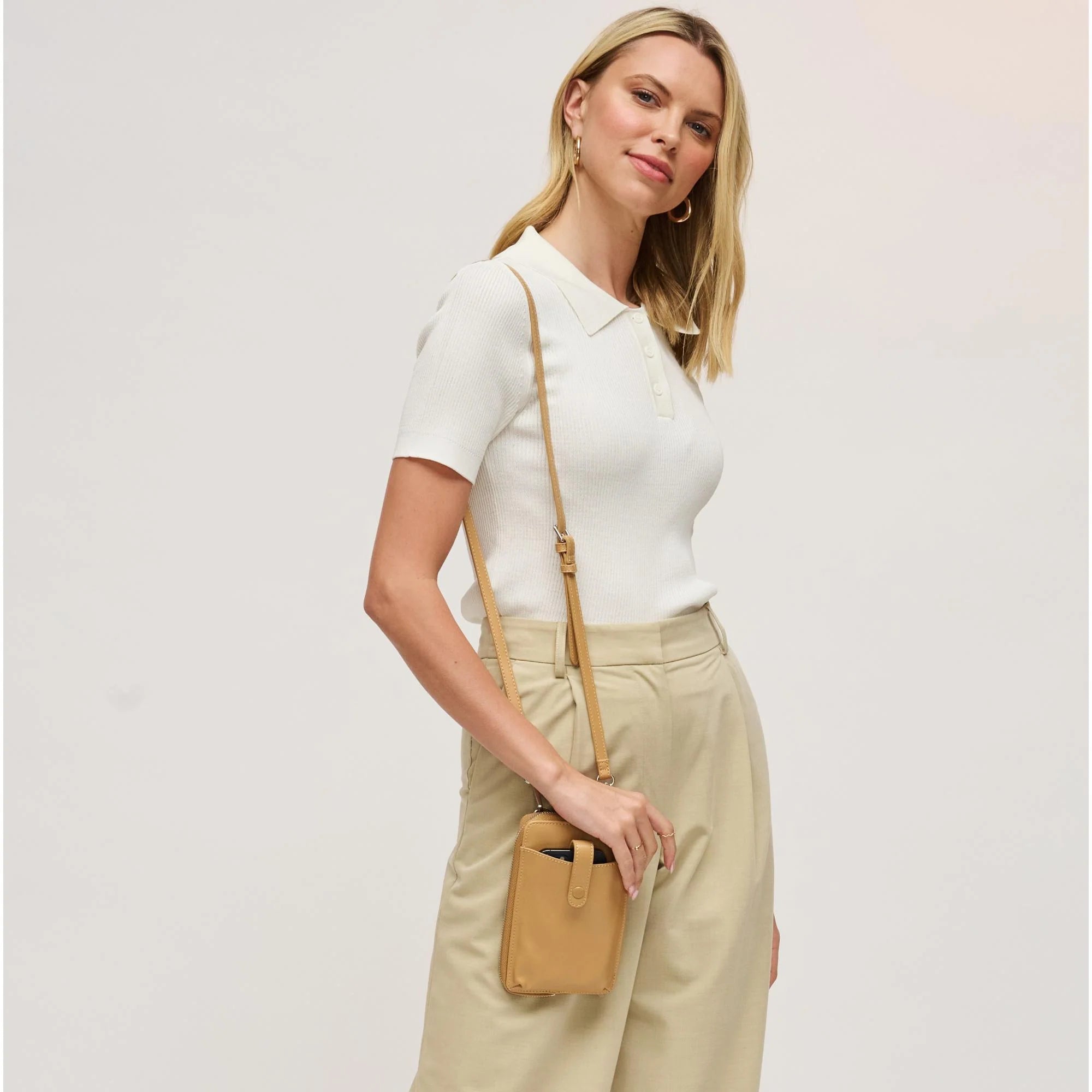 Woman with a tan cell phone wallet crossbody against a white background
