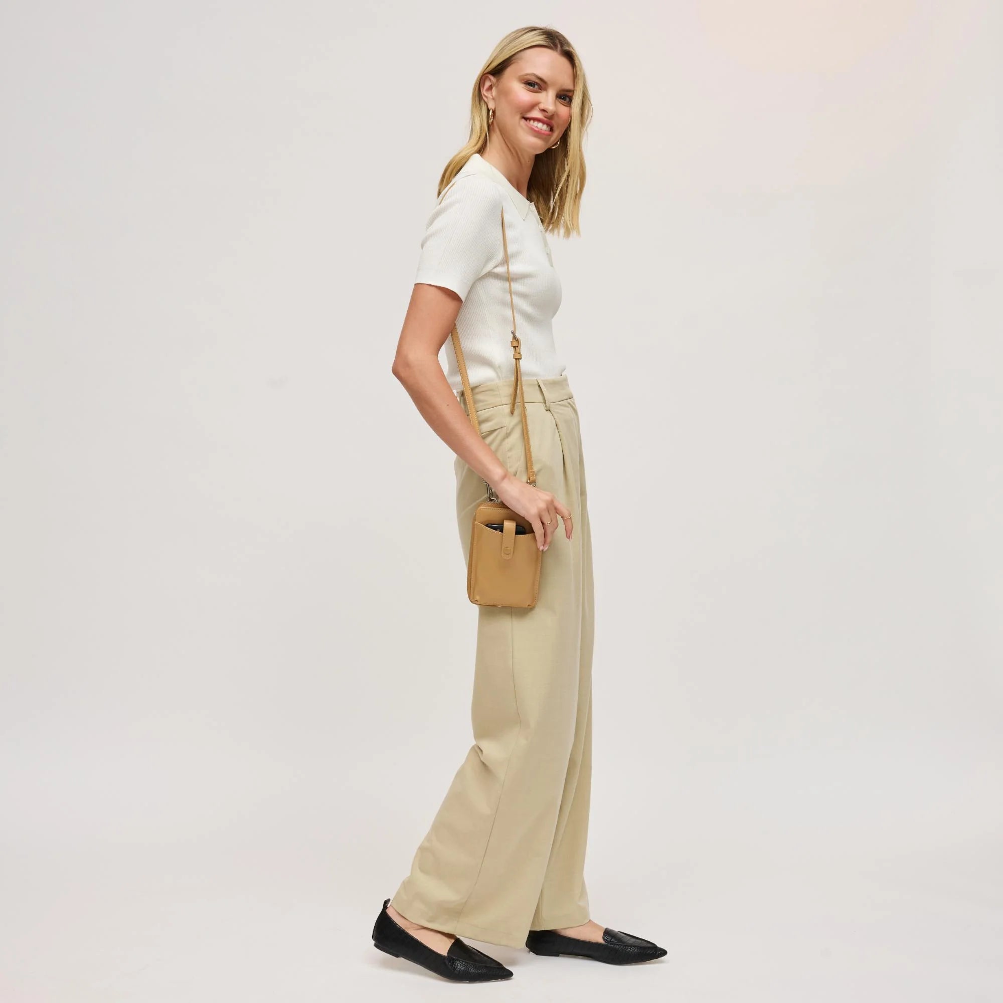 Woman with a tan cell phone wallet crossbody against a white background