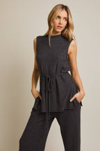 Woman wearing a heather gray sleeveless top and pants against a beige background