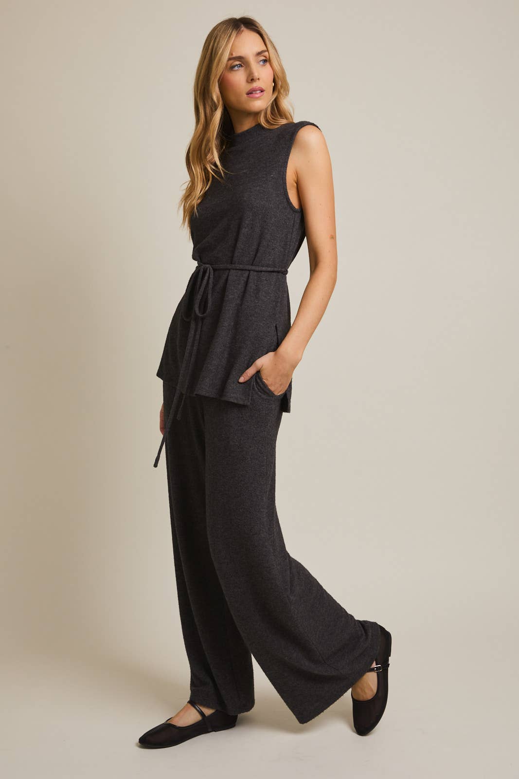 Woman wearing a heather gray sleeveless top and wide-leg pants on a beige background