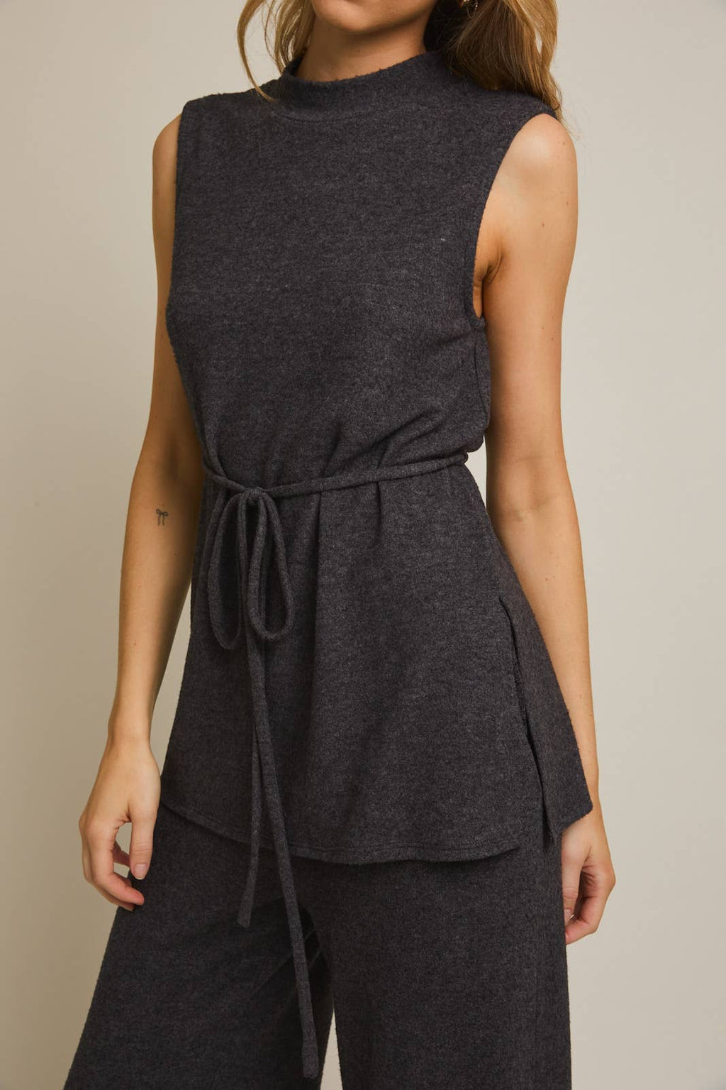 Woman wearing a heather gray sleeveless top and pants on a beige background