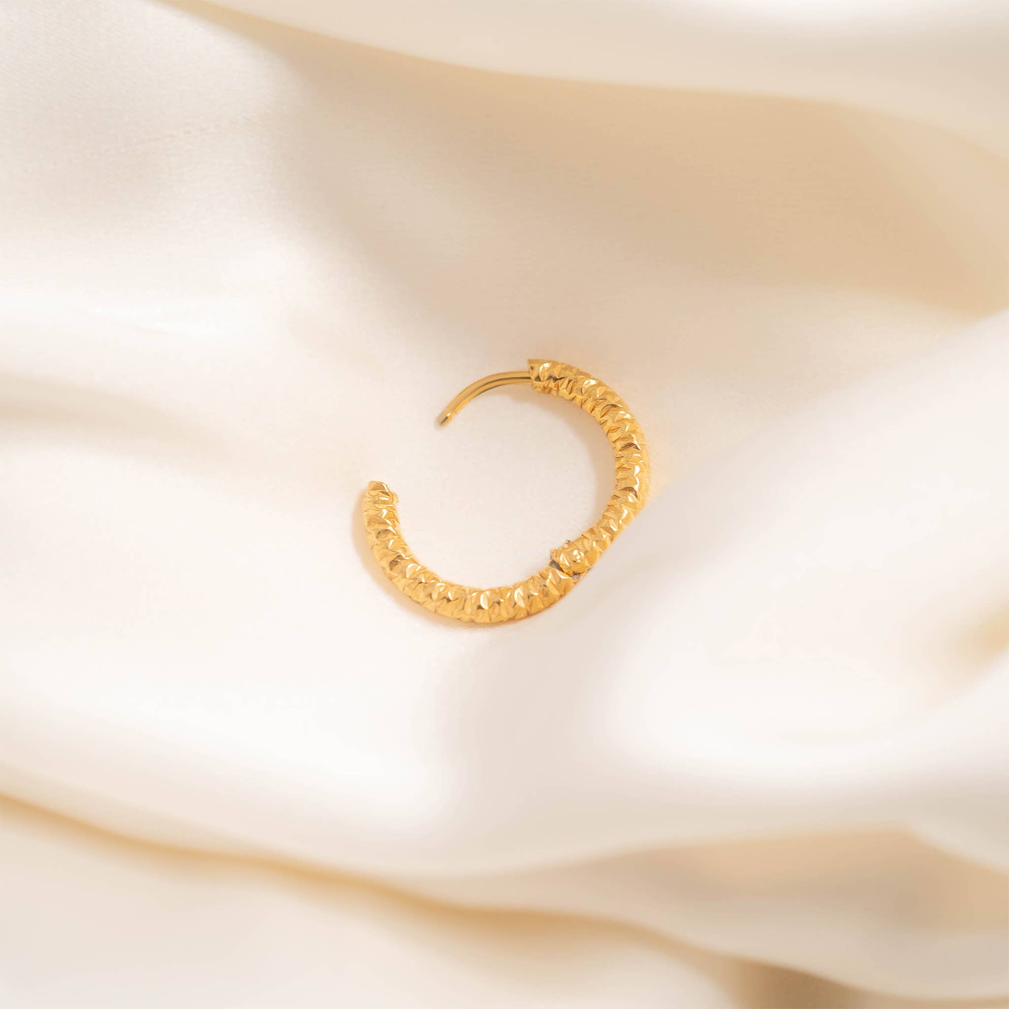 Gold huggie hoop earring on a soft beige fabric background