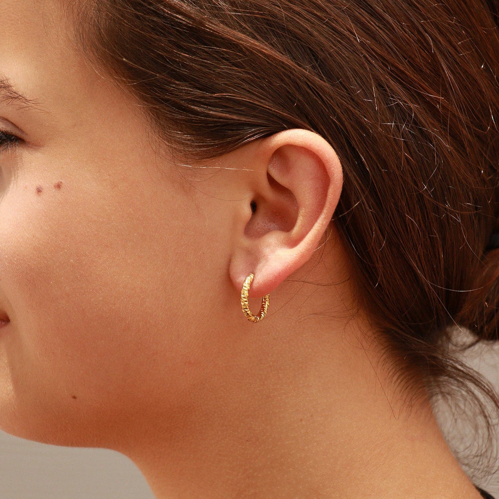 Close-up of a person wearing a gold huggie hoop earring.
