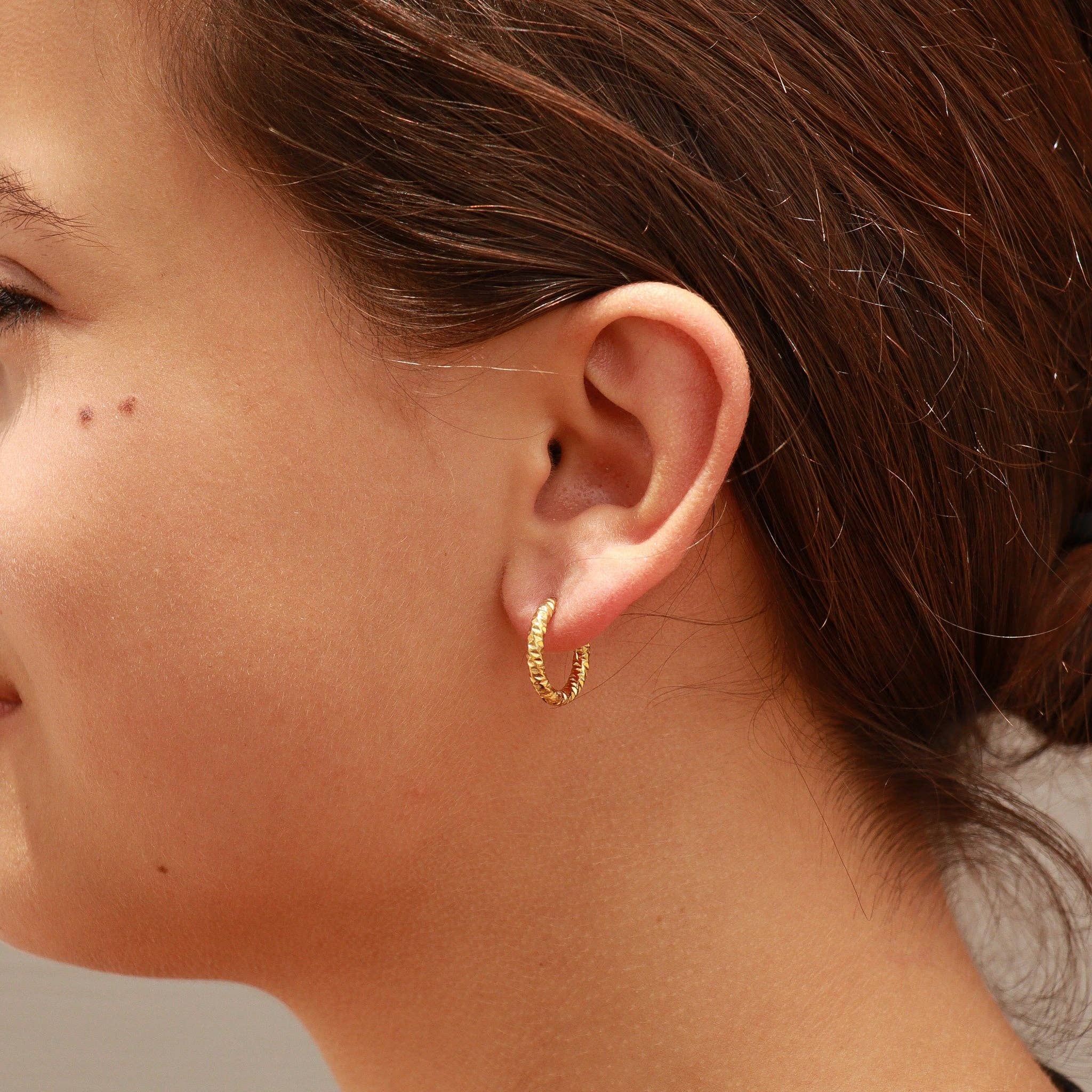 Close-up of a person wearing a gold huggie hoop earring.