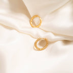 Gold huggie hoop earrings on a soft beige fabric background