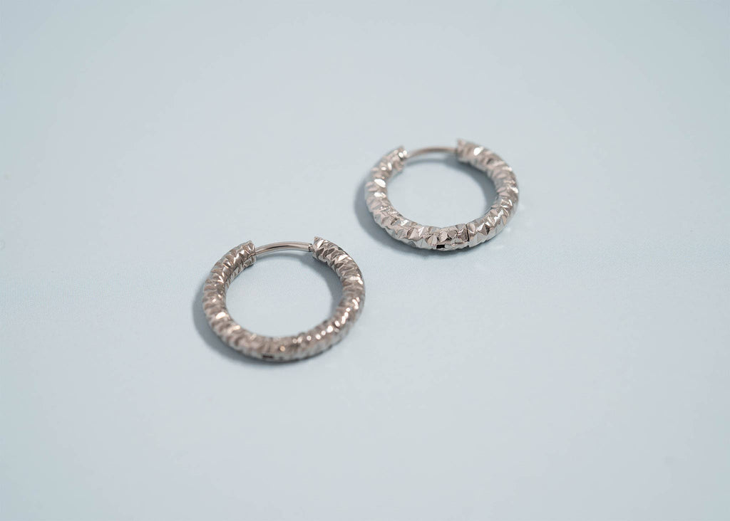 Pair of silver textured hoop earrings on a light blue background