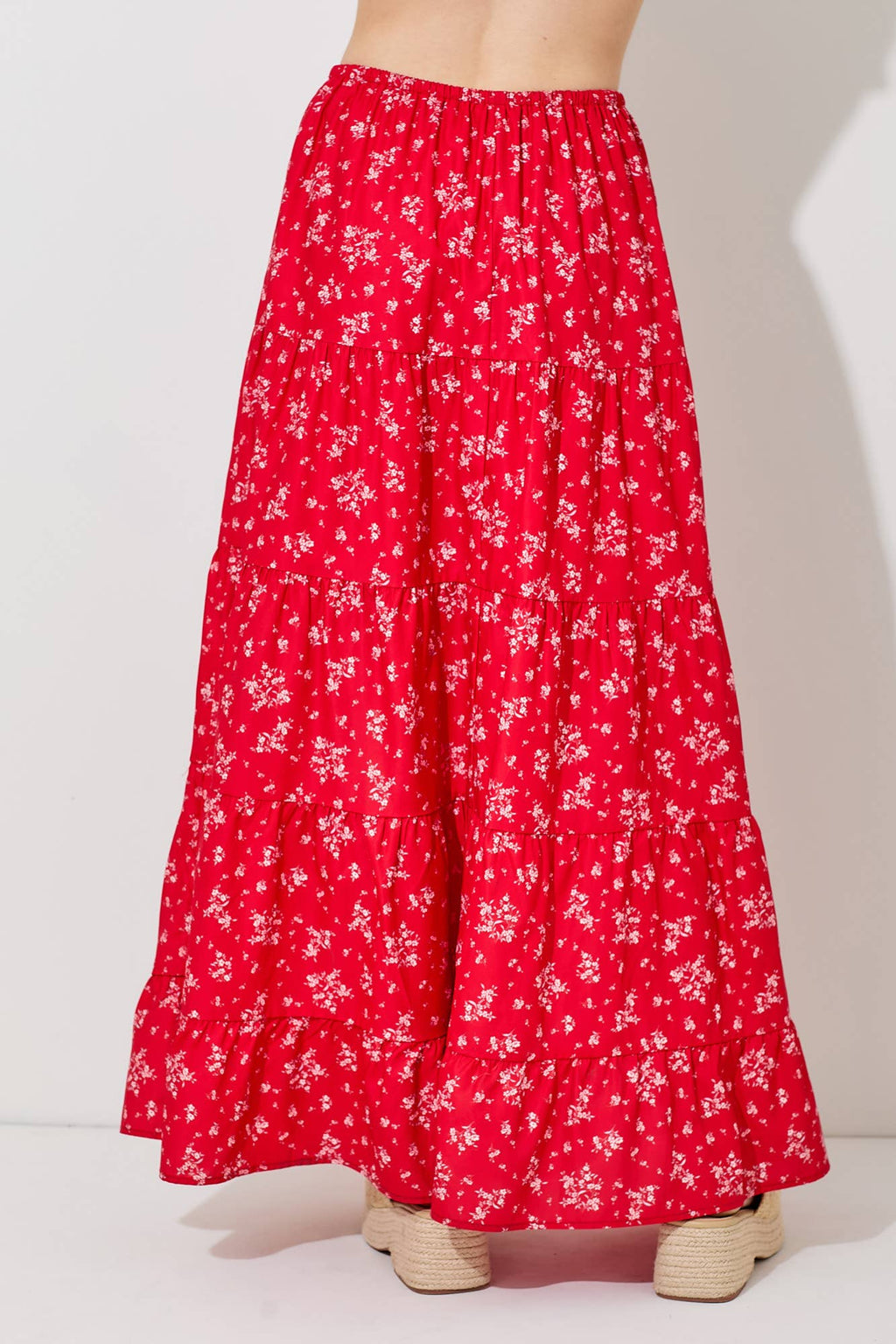 Woman wearing a floral print tiered red skirt against a gray background