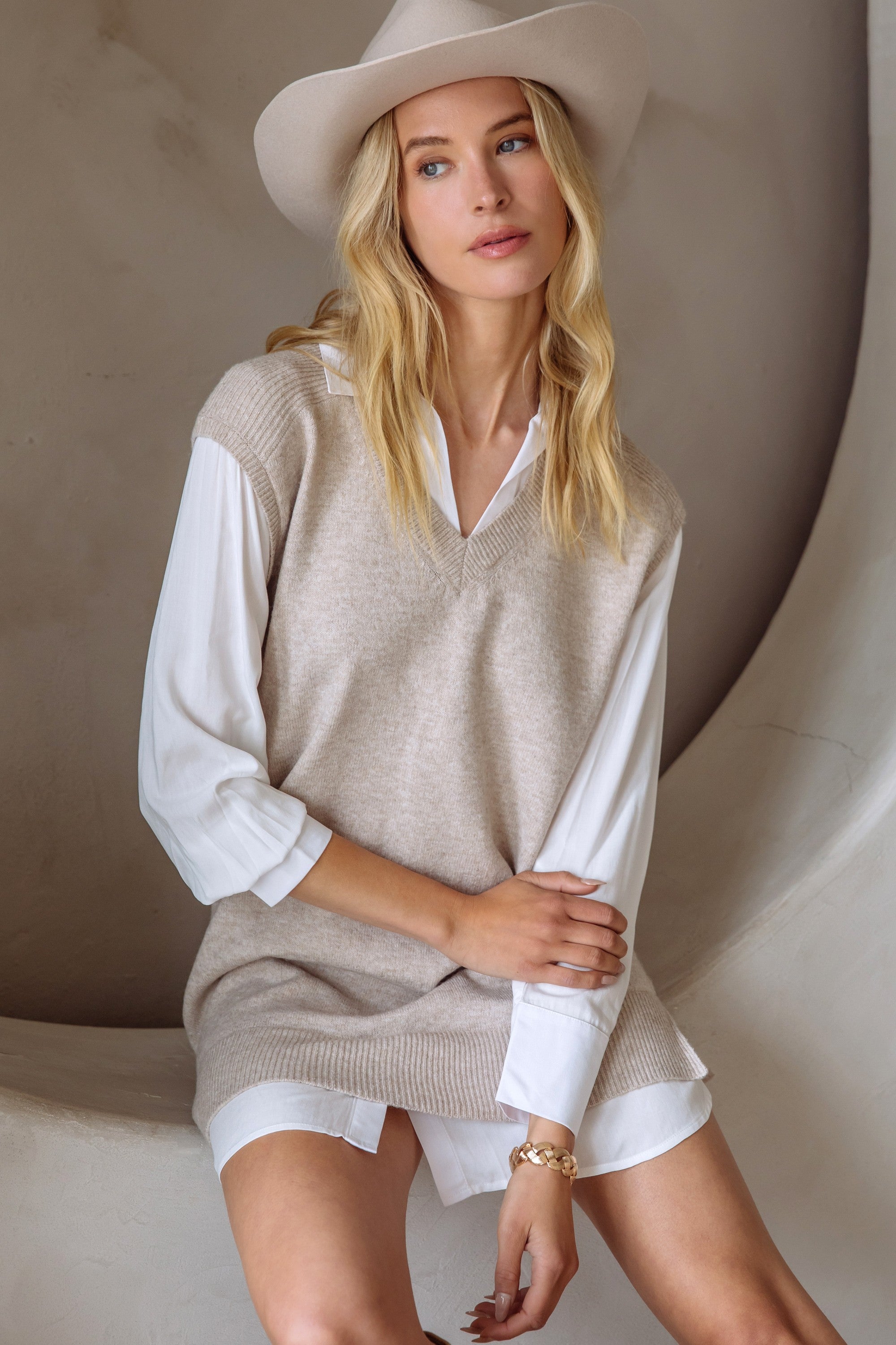Woman in a beige and cream layered shirt dress and boots standing next to a neutral wall