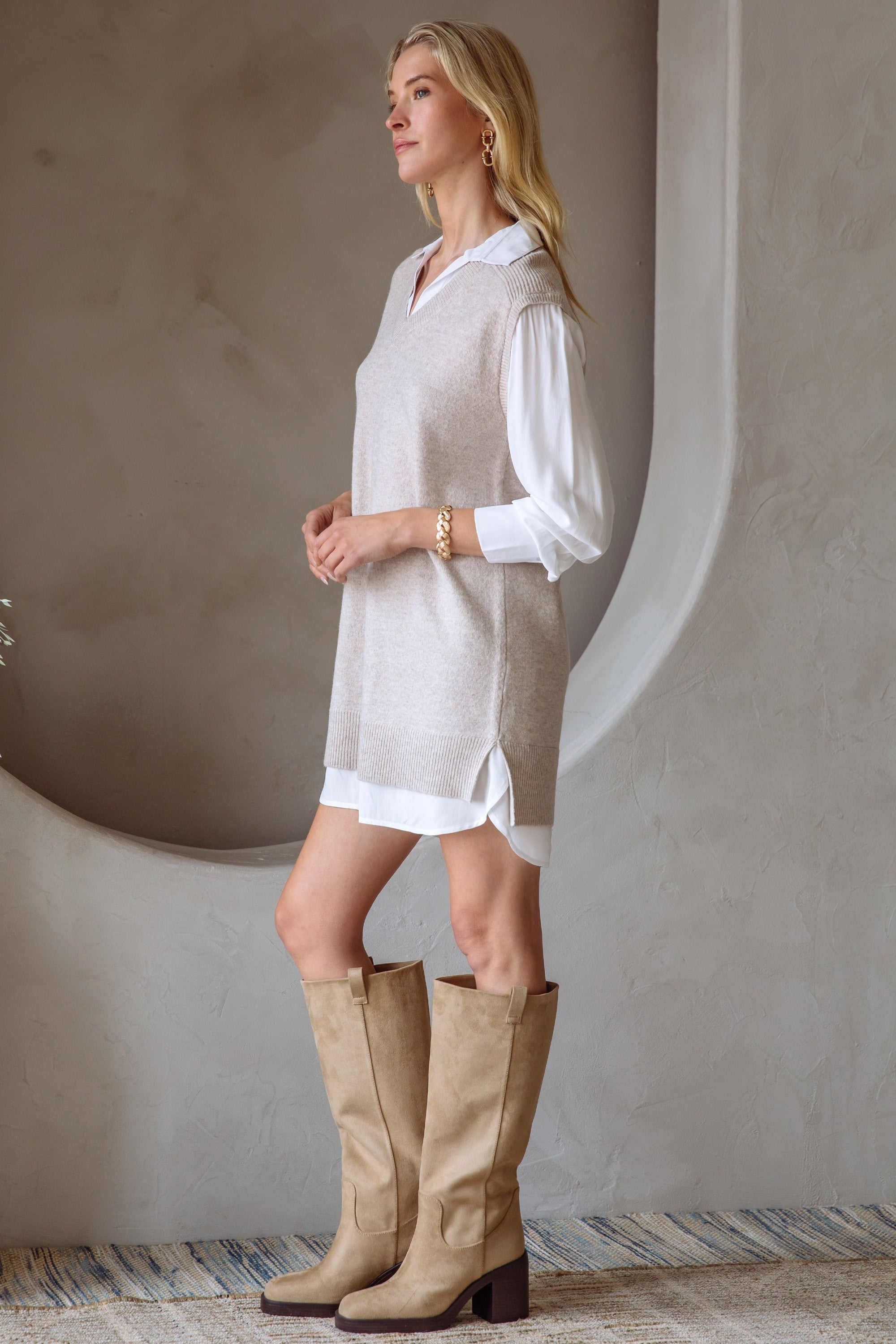 Woman in a beige and cream layered shirt dress and boots standing next to a neutral wall